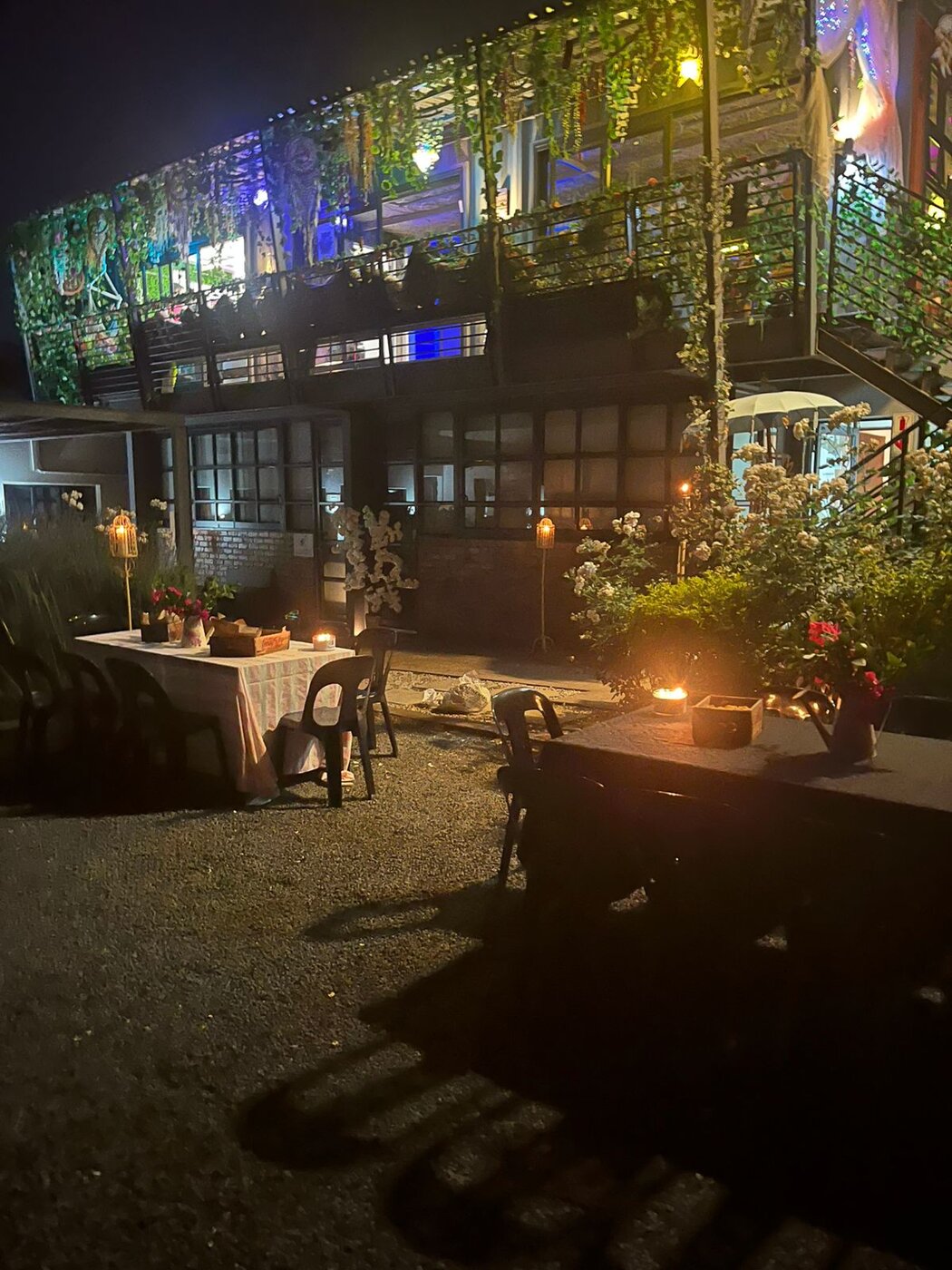 The HappiSpace venue lit at night with a candlelit dinner table set in the garden, Fairmount